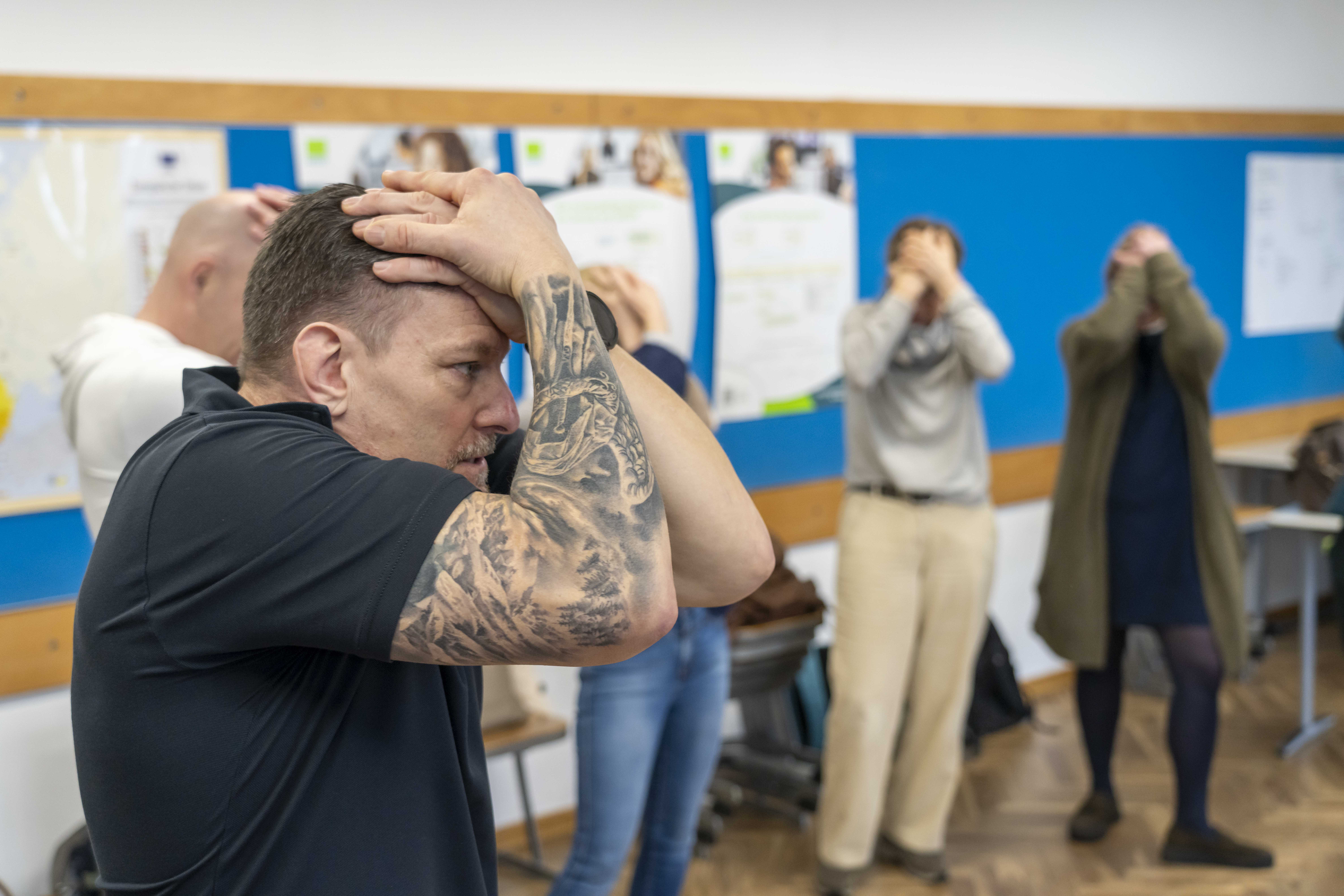 Ein Mann im schwarzen T-Shirt hält seine tätowierten Arme schützend vor seine Stirn